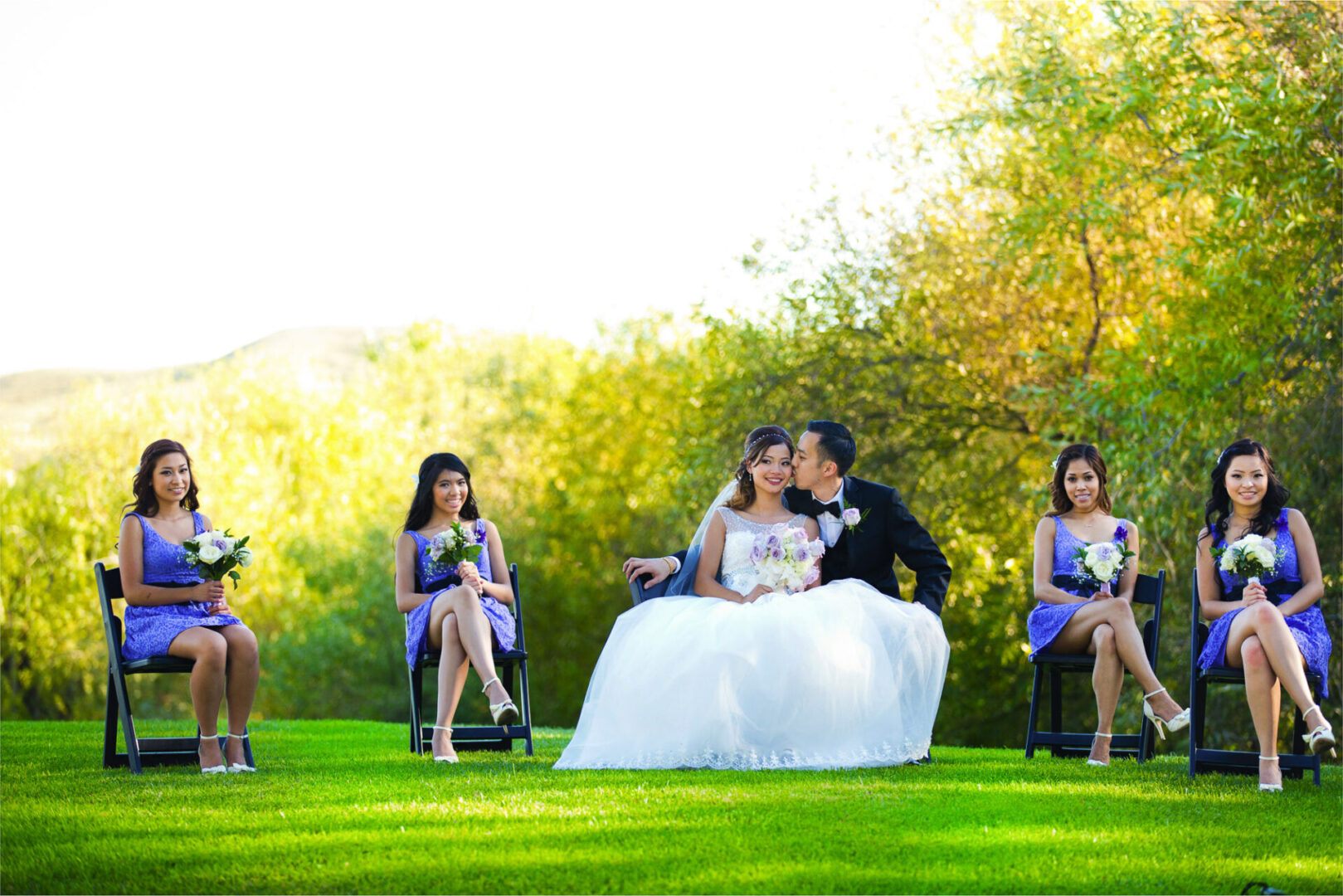 A couple kissing in a field along with girls sitting on the chair