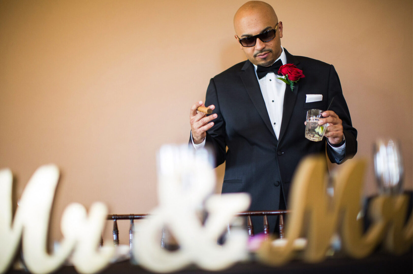 A groom holding a glass of drink and cigar in hand