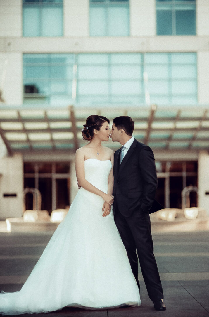 A newly married couple kissing near a building